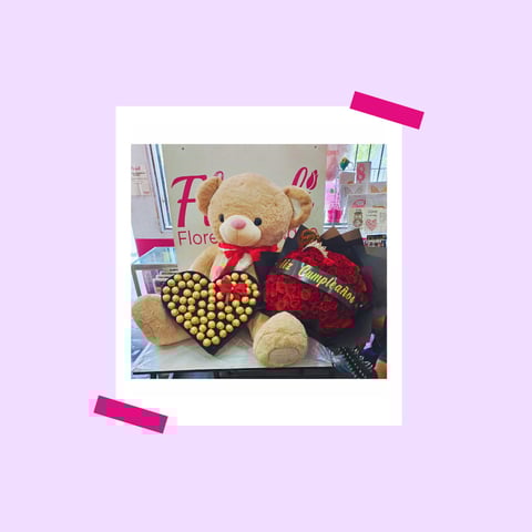 Tan teddy bear holding a gold and red heart-shaped box with red fabric, displayed on lavender background with pink tape