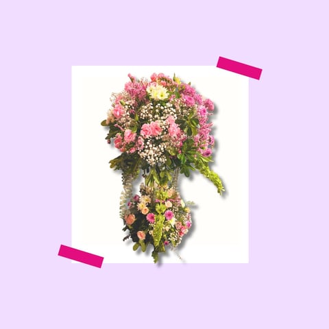 Floral arrangement with pink carnations, white filler flowers, and cascading greenery in a vase on a lavender background