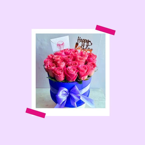 Polaroid-style photo of pink roses in a blue vase with purple ribbon and Happy Birthday topper on lavender background