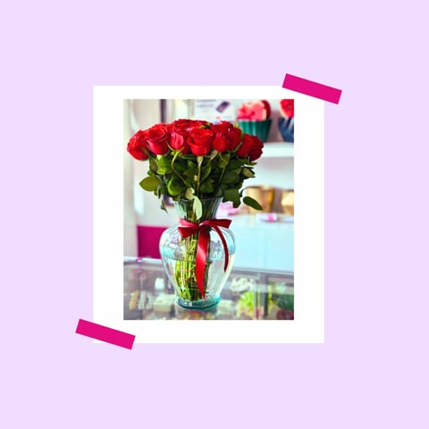Bouquet of red roses in a clear glass vase with red ribbon, displayed on a light background with decorative tape